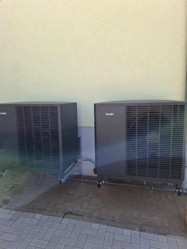 Zwei dunkle Luft-Wasser-Wärmepumpen nebeneinander an einer Hauswand.