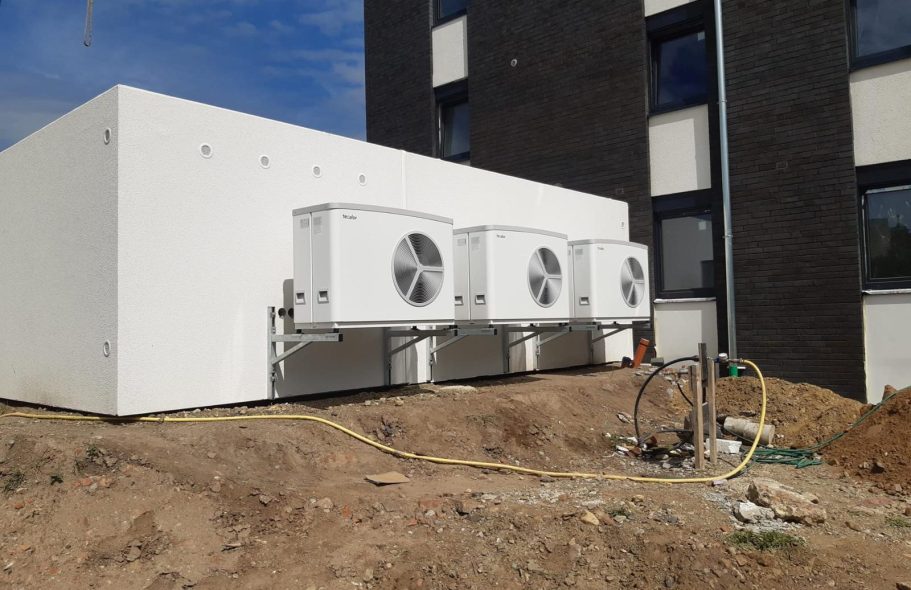 Wärmepumpenanlage mit mehreren Außengeräten Mehrere Luft-Wasser-Wärmepumpen vor einem Mehrfamilienhaus als Beispiel für eine größere Heizungsinstallation.