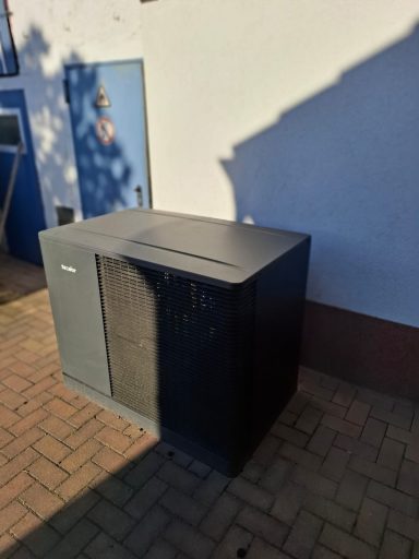 Kompakte dunkle Luft-Wasser-Wärmepumpe direkt am Wohngebäude.