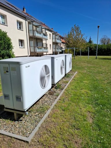 Zwei große Luft-Wasser-Wärmepumpen im Außenbereich eines Mehrfamilienhauses.